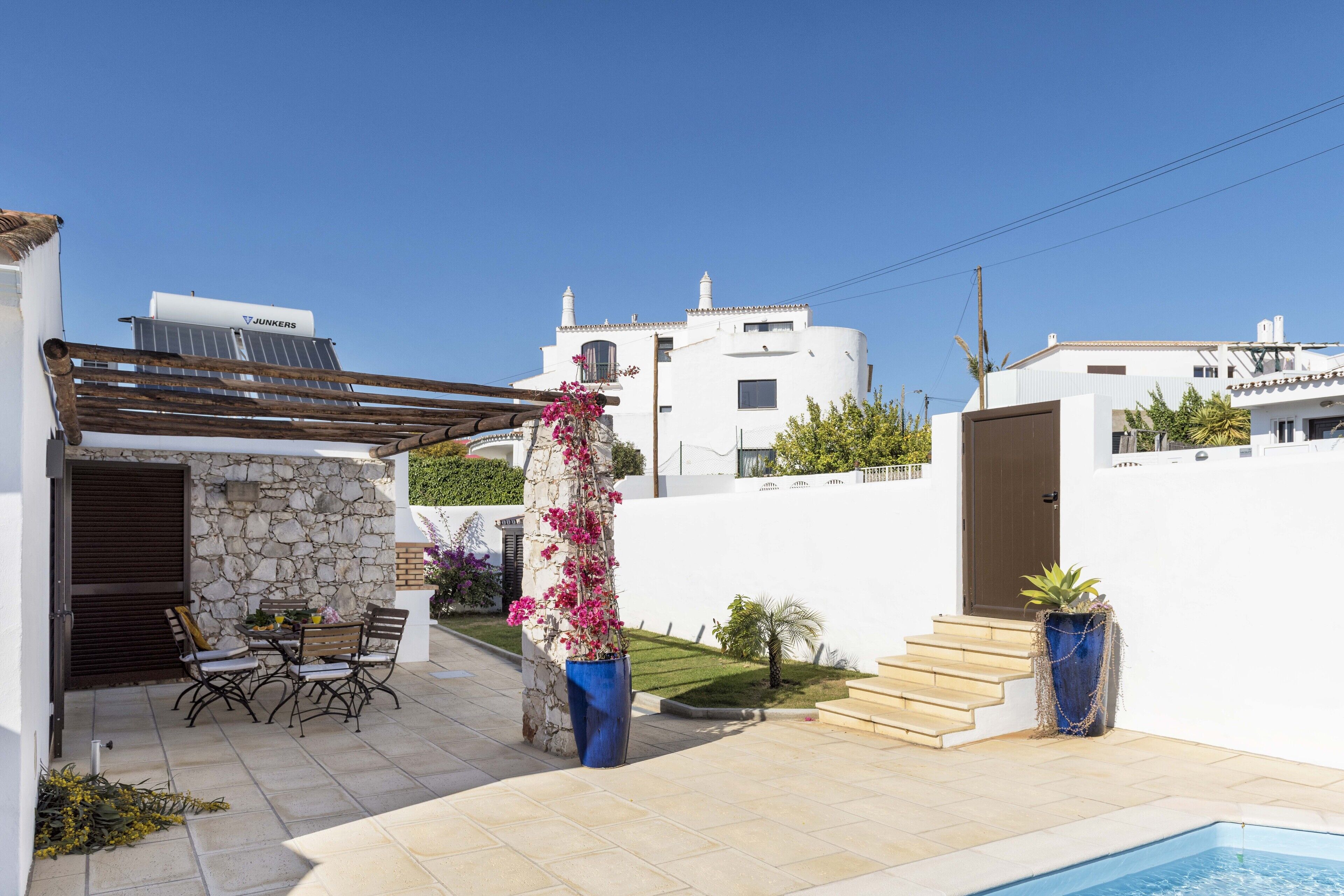 Une terrasse avec des meubles d’extérieur, un mur en pierre, une pergola et une piscine.