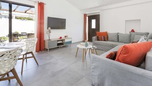 Un saló modern amb un sofà gris, cadires blanques, una taula rodona petita i un televisor penjat a la paret.