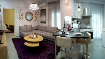 A modern living room with a sofa, a dining table with chairs, and a kitchen area with appliances.