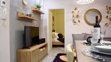 A modern living room with a TV, wooden shelves, a dining table set with plates, and a wine bottle.