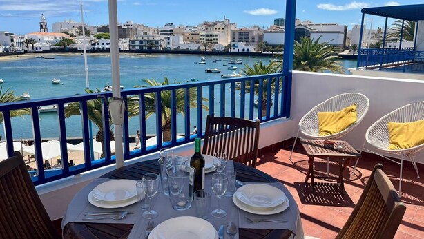 A terrace with a table set for dining, overlooking a marina with boats and buildings in the background.