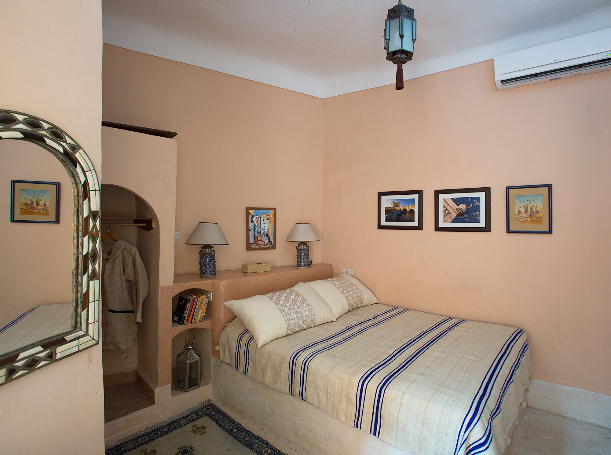 A bedroom with a bed, bedside lamps, a mirror, a wardrobe, and framed pictures on the wall.