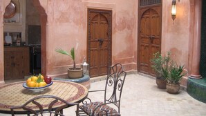 Een traditioneel Marokkaans interieur met een ronde tafel, stoelen, een fruitschaal en houten deuren.