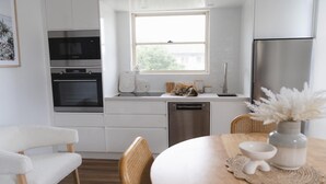 Una cocina moderna con armarios blancos, horno empotrado, microondas y refrigerador de acero inoxidable.