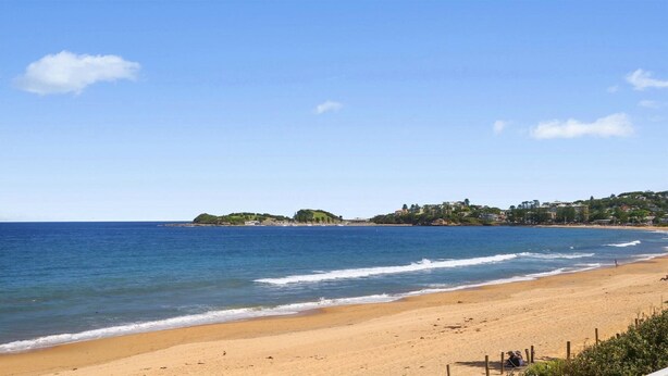 Una playa con agua azul cristalina, orilla de arena y un pueblo al fondo.