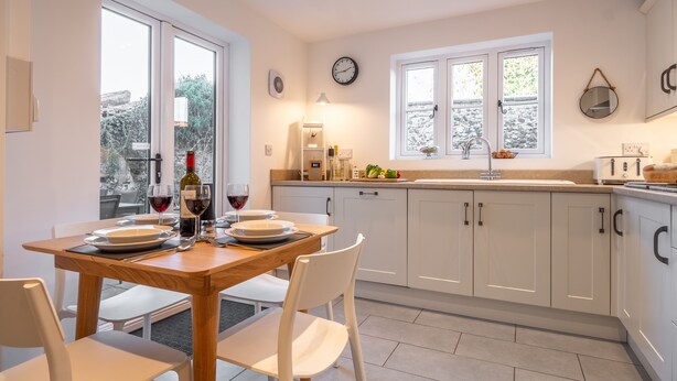 Une cuisine moderne avec des meubles blancs, une table à manger en bois et une fenêtre donnant sur des arbres.