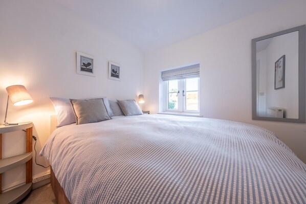 Une chambre à coucher avec un lit, des lampes de chevet, une fenêtre avec des rideaux et deux tableaux accrochés au mur.