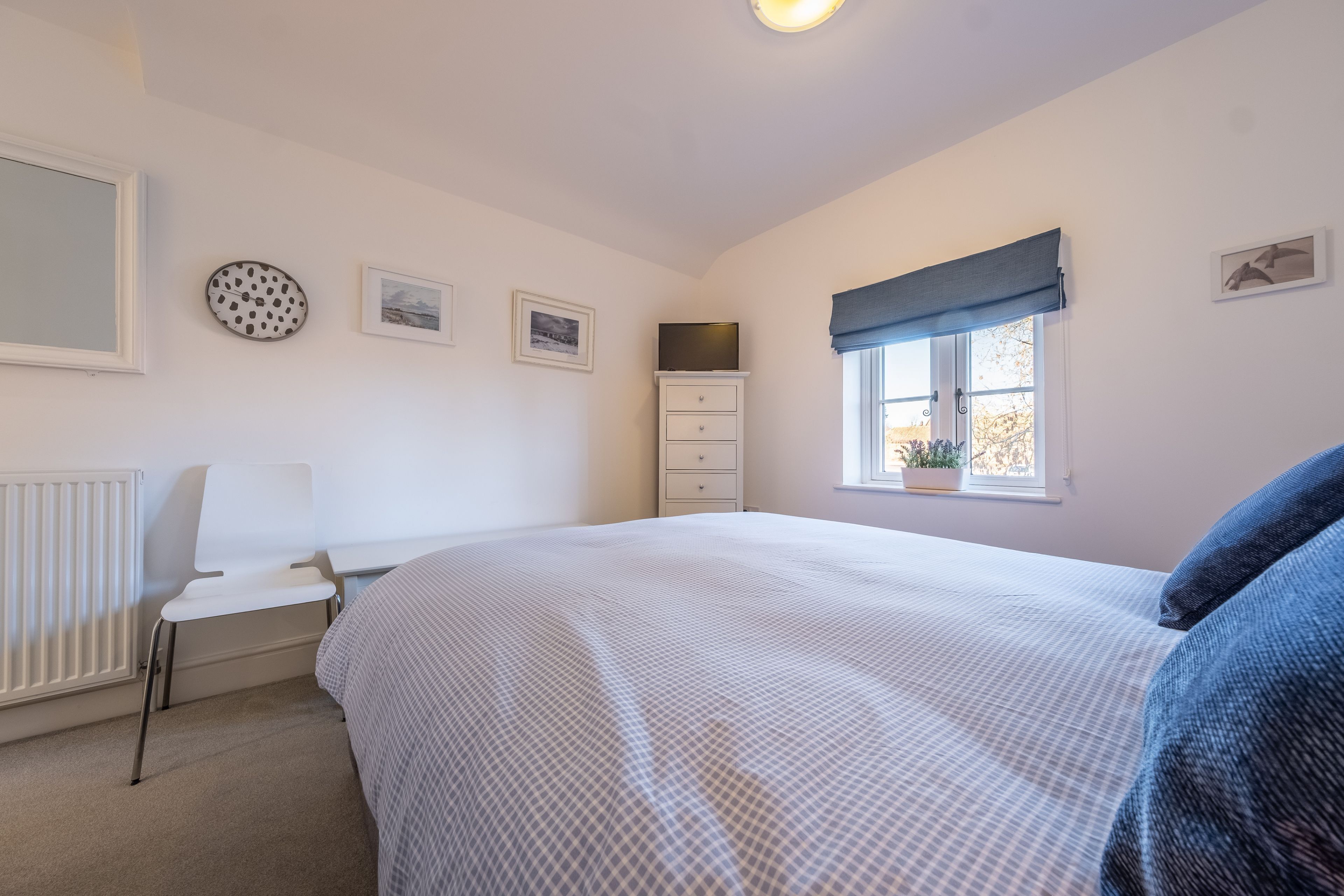 Een slaapkamer met een bed, een stoel, een dressoir, een raam met uitzicht en wanddecoraties.