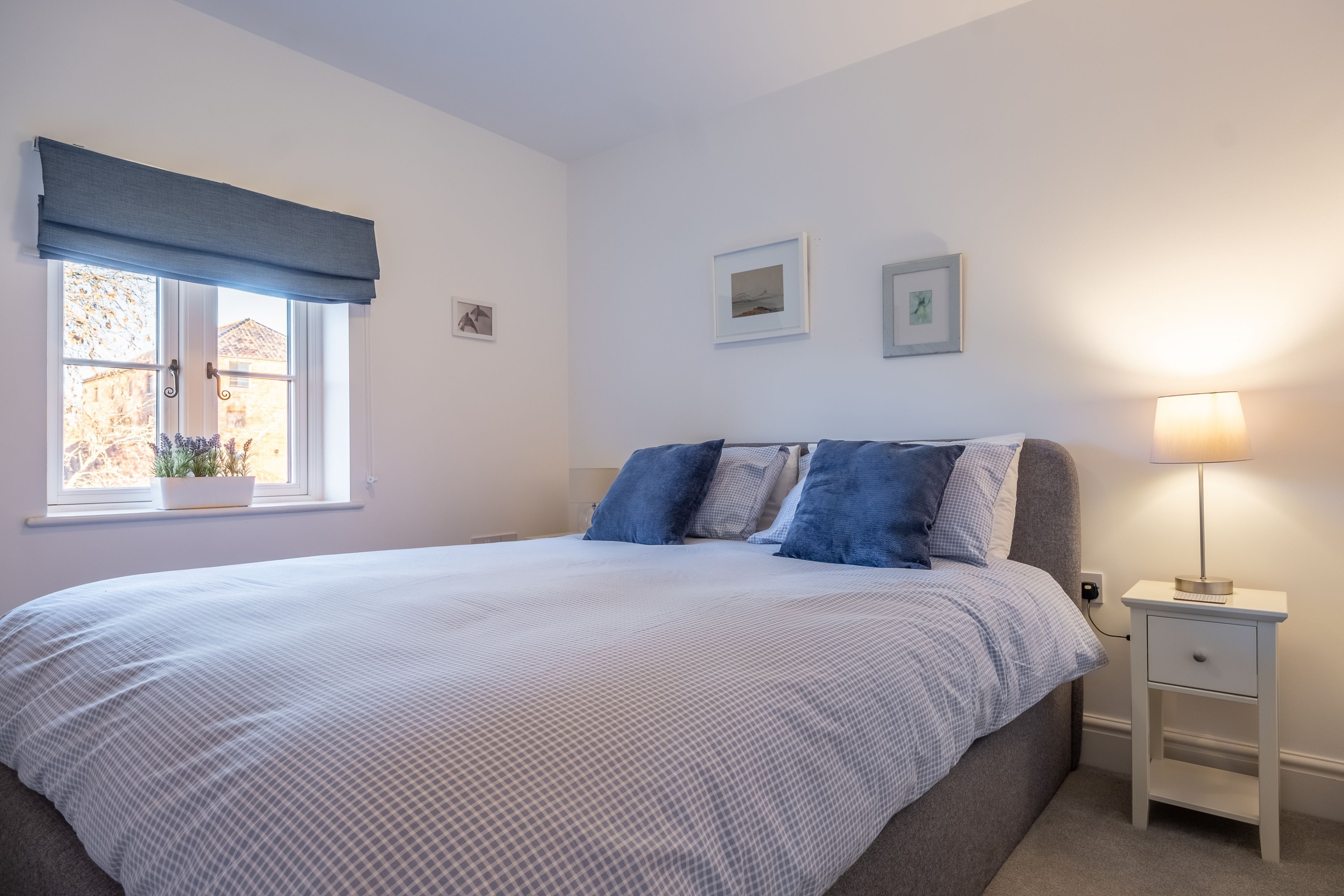 Une chambre à coucher comprenant un lit, une table de chevet, une lampe, une fenêtre avec vue et des œuvres d’art murales.