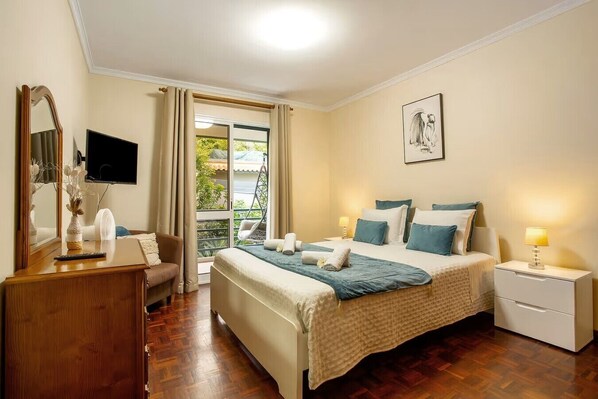 A hotel room with a bed, bedside tables, a desk, a chair, a TV, a window with curtains, and a balcony view. - Madeira Funchal Gardens  (Funchal)