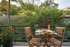 A dining table with chairs, breakfast items, and a bottle of orange juice on a balcony with a view of greenery and buildings. - Madeira Funchal Gardens  (Funchal)