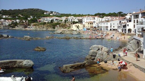 A coastal town with a rocky beach, clear blue water, and white buildings.