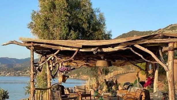 A rustic outdoor seating area with wooden loungers and a pergola structure, overlooking a body of water and hills. - House / Villa - VILLANOVA (Villanova)