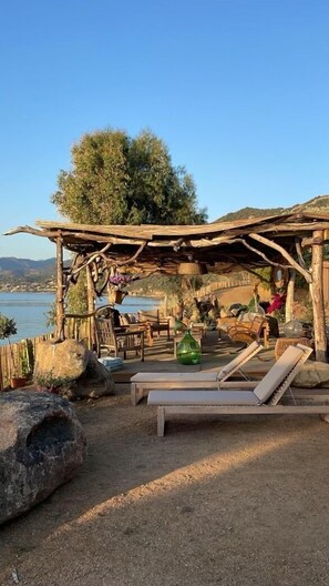 A rustic outdoor seating area with wooden loungers and a pergola structure, overlooking a body of water and hills. - House / Villa - VILLANOVA (Villanova)