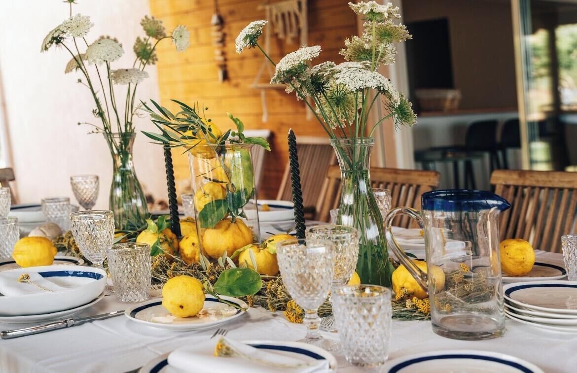 Ein Tisch ist gedeckt mit Geschirr, Tellern und Blumen, mit Holzvertäfelung im Hintergrund und Stühlen.