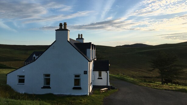 A white house with a chimney, a small porch, and a road leading to it.