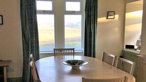 A dining room with a round table, six chairs, a bowl, and a view through large windows.