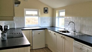 A compact kitchen with white cabinets, a black countertop, a built-in dishwasher, and two windows providing natural light.