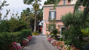 A cobblestone pathway leading to a building with a pink facade, surrounded by lush greenery and flower beds. - Villa Raffaela - Stately home, independent, quiet, sunny, ideal for a relaxing holiday (Ercolano)