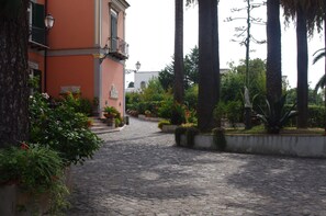 A cobblestone street with a building on the left and a garden with palm trees on the right.