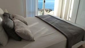 Una cama con colchón blanco, manta gris y dos almohadas.