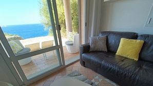 Una sala de estar con un sofá de cuero, una mesa de centro con una flor, y vista al mar a través de amplios ventanales.
