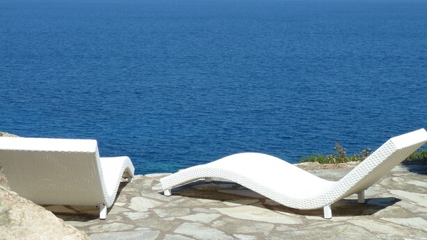 Dos sillones blancos en un patio de piedra con vistas al mar.
