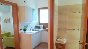 A compact kitchen with a microwave, sink, and a small wooden stool with towels.