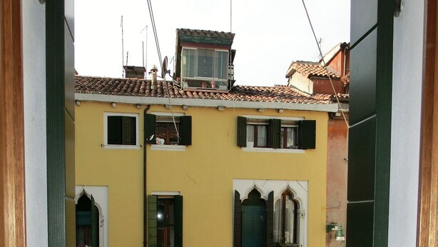 A yellow building with multiple windows and balconies, a visible door, and a brick-paved courtyard.