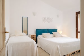 A bedroom with two beds, a mirror, wall sconces, and a small wooden side table.