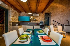 Un comedor con pared de piedra, vigas de madera en el techo y una cocina al fondo.