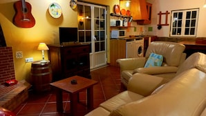A cozy living room with a sofa, a small table, a television, and a guitar hanging on the wall. - Where the nature and the welfare are find in full harmony (Vila Nova de Milfontes)