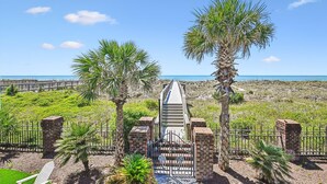 A pathway leading to a gated entrance with palm trees and a view of the beach. - Isle Of Palms, Luxury Oceanfront Home with Hot Tub (NORTH MYRTLE BEACH)
