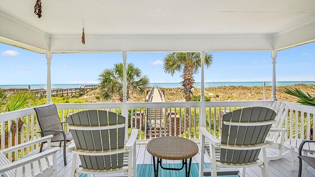 A covered outdoor area with white railings, three Adirondack chairs, a small round table, and a view of the beach and ocean. - Isle Of Palms, Luxury Oceanfront Home with Hot Tub (NORTH MYRTLE BEACH)