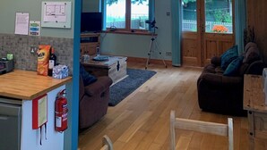 A spacious living area with a high ceiling and wooden beams, a cozy seating area with a couch and chairs, a kitchen area with a counter and appliances, and a view of the outdoors through windows. - Scottish Highlands Invergordon By NC500 Route Minimum 3 nights Any Start Day (Invergordon)