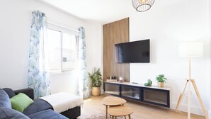 A modern living room with a sofa, a small wooden table, a TV mounted on a wall, and a floor lamp. - Home2Book Vibrant & Trendy Apt Santa Cruz Center (Santa Cruz de Tenerife)