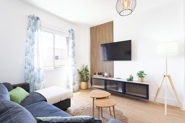 A modern living room with a sofa, a small wooden table, a TV mounted on a wall, and a floor lamp.