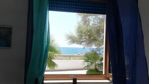 Una ventana con vista a una carretera costera, palmeras y un cielo azul despejado.