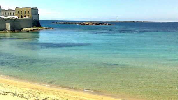 Escena costera con una playa despejada, un edificio fortificado y un faro distante.