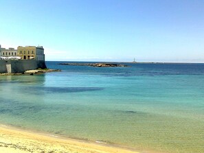 A coastal scene with a clear beach, a fortified building, and a distant lighthouse. - Beachfront villa a few kilometers from Gallipoli and every tourist attraction. (Capilungo)