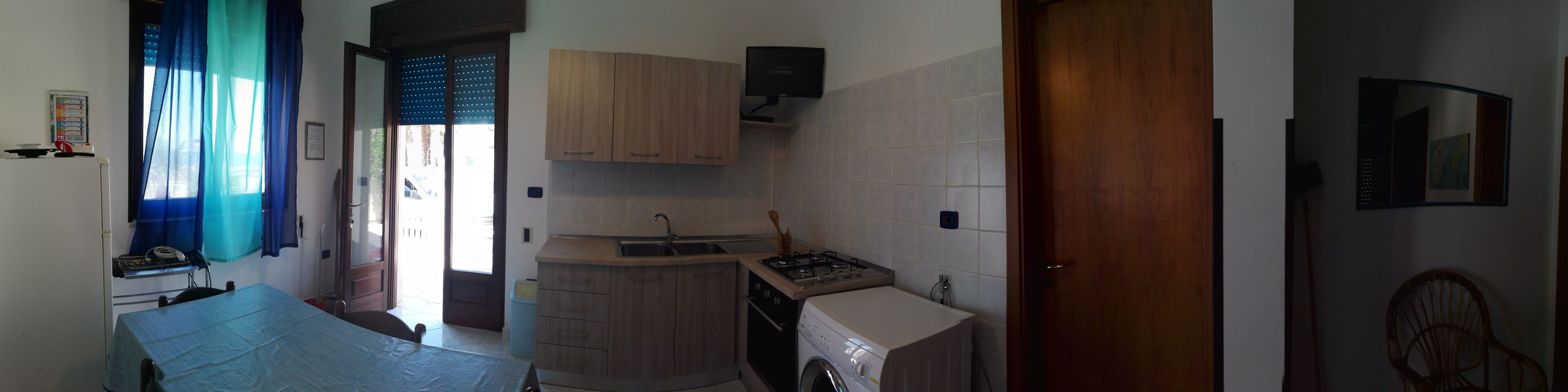 Een kleine keuken met een spoelbak, kastjes en een wasmachine.