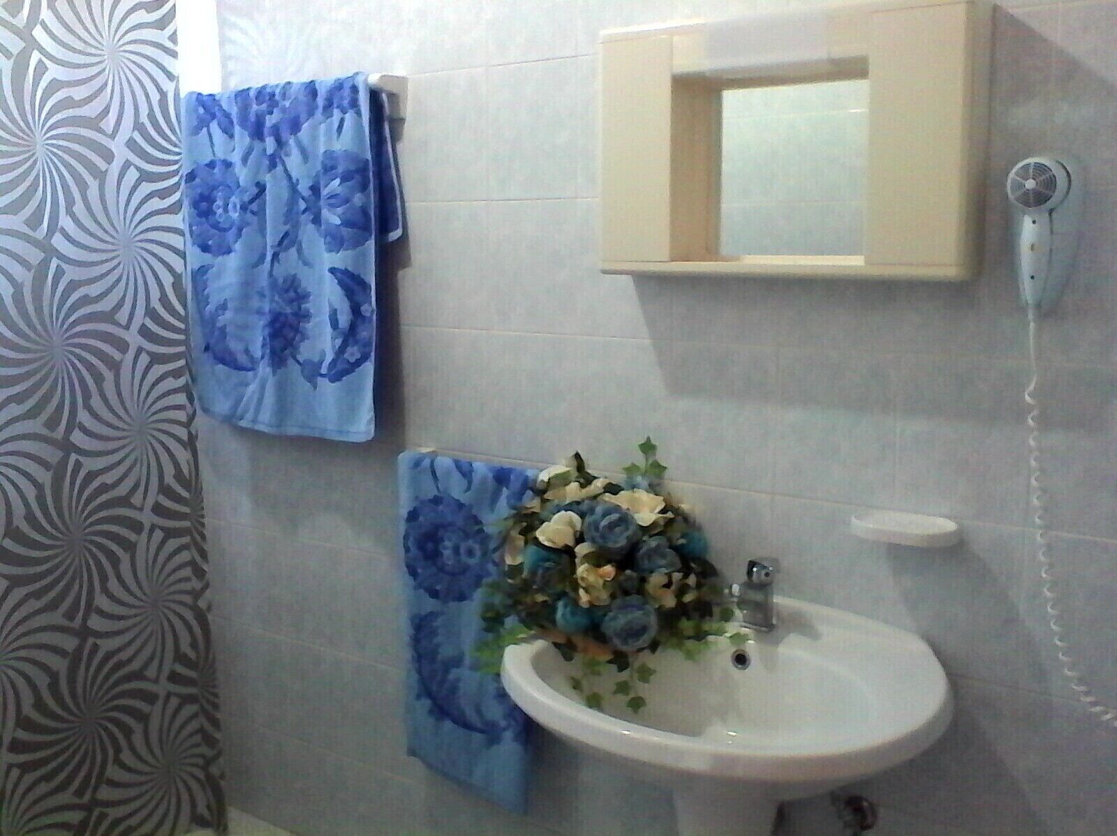 A bathroom with a white sink, a mirror, and a towel rack with a blue floral towel.