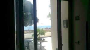 Habitación con puerta corrediza de vidrio que da a un espacio exterior con mesa y sillas, vista al mar y una pequeña palmera.
