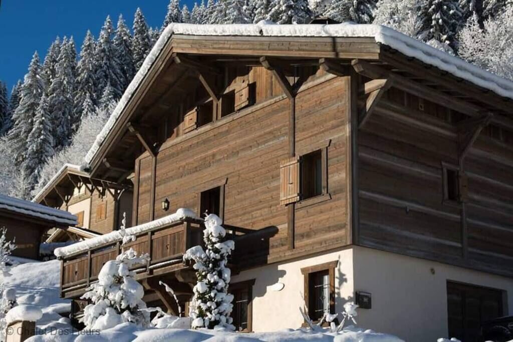 A wooden chalet with a balcony, surrounded by snow-covered trees.
