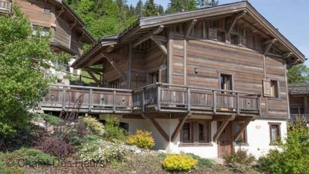 Un chalet en bois doté d’un balcon, entouré de verdure et d’arbres.