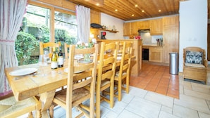 Une table à manger en bois avec des chaises, un coin cuisine avec des meubles en bois, et une vue sur la verdure à l’extérieur.