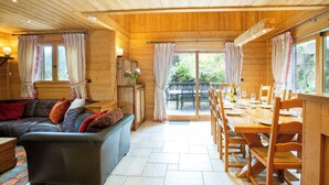 L’intérieur chaleureux d’un chalet avec un coin repas en bois, un canapé en cuir et une grande fenêtre.