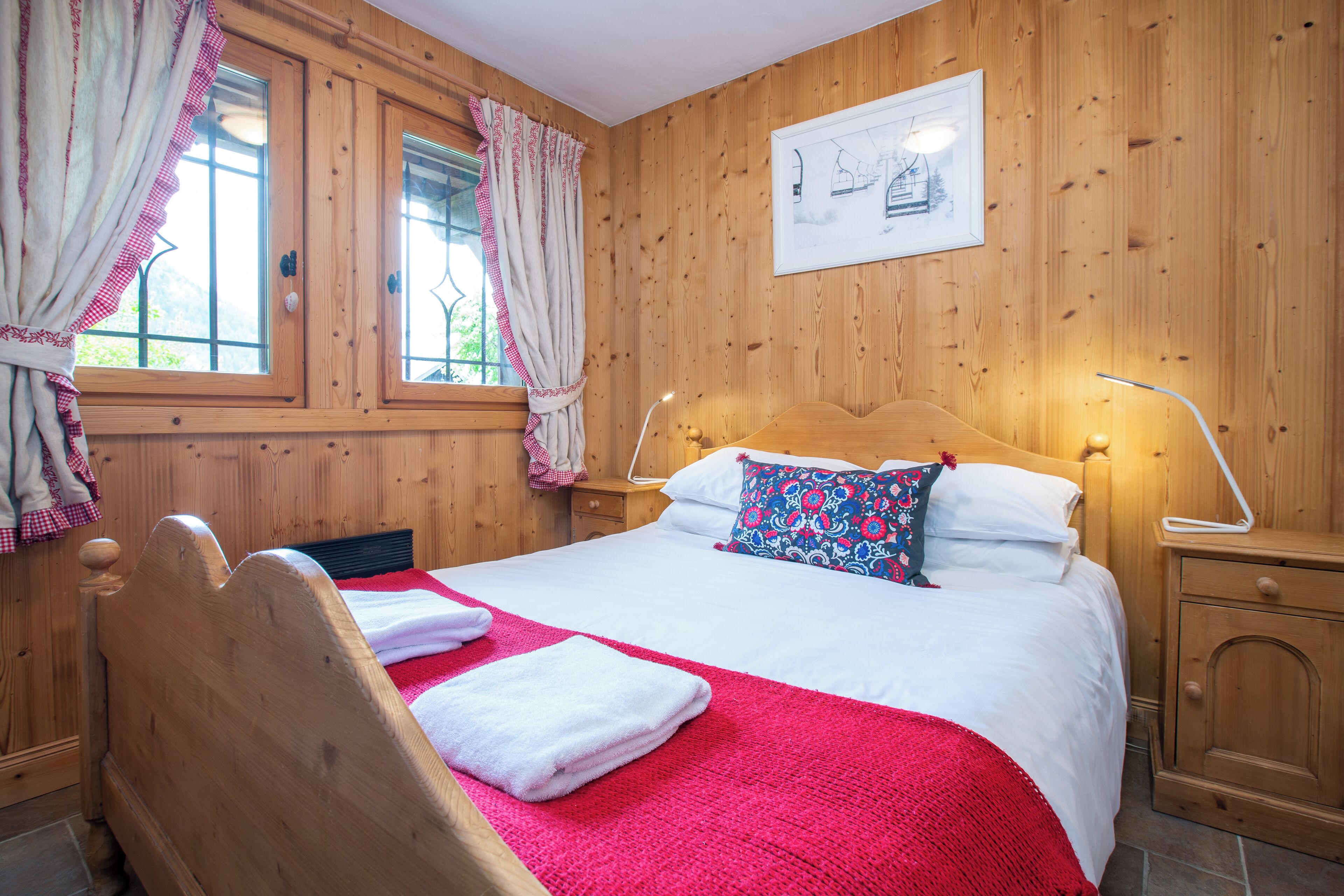 A wooden-paneled bedroom with a bed, curtains, a nightstand, and a framed picture on the wall.