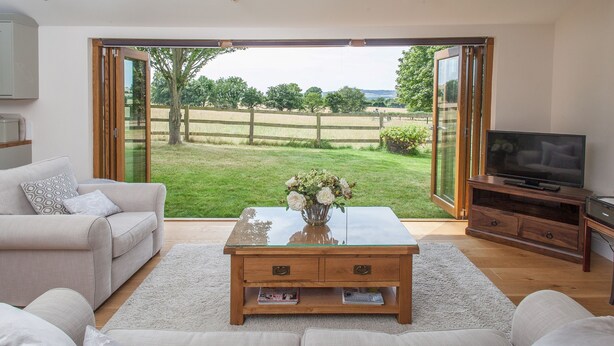 A living room with a glass coffee table, sofa, and TV stand. - Romantic and peaceful cottage With Far Reaching Views  (West Meon)