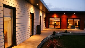 A modern house with a wooden deck, large windows, and a well-lit interior. - Single-storey house, close to the port and Kerdéniel beach. (Ploudalmézeau)
